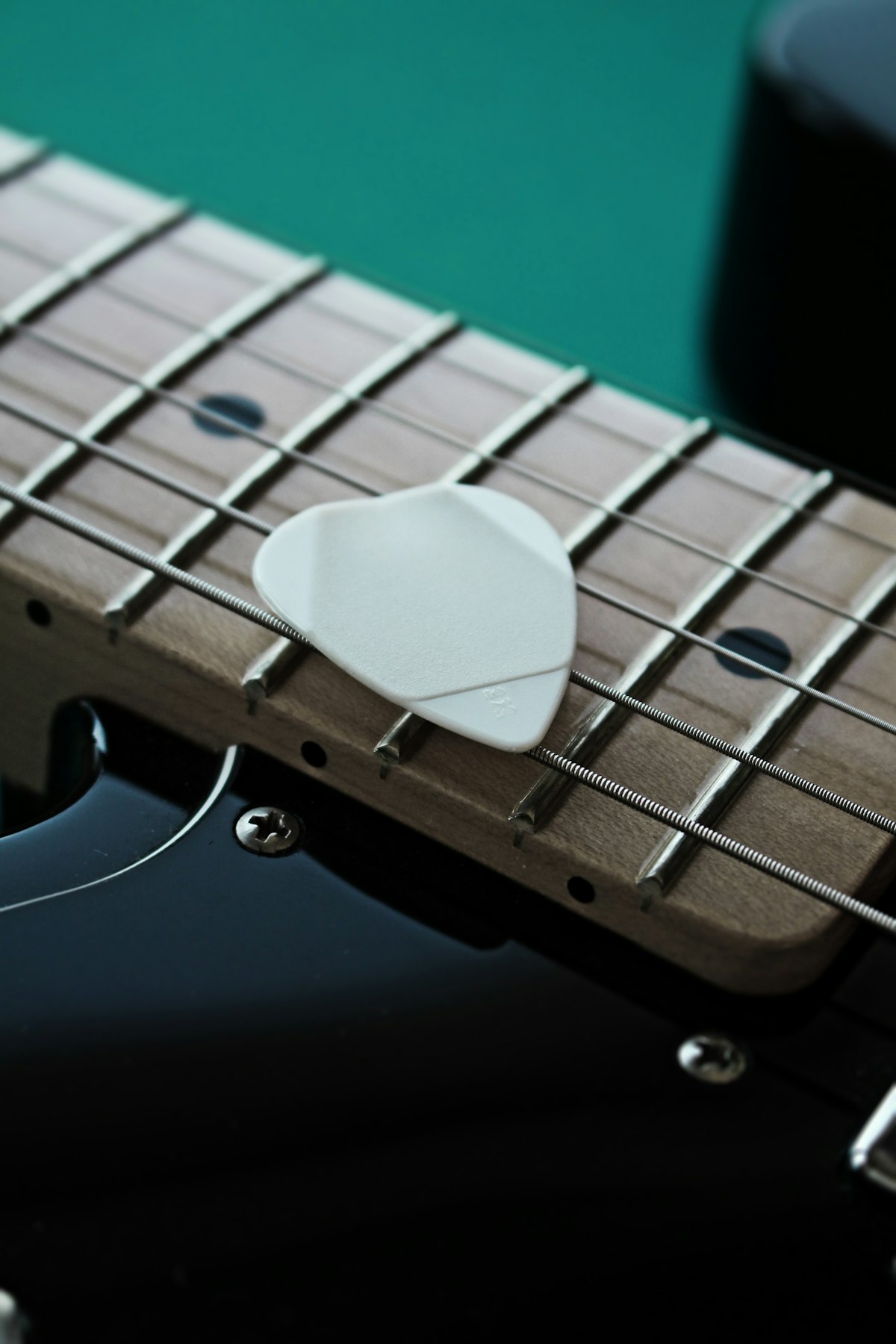 A white guitar pick resting on an electric guitar fretboard